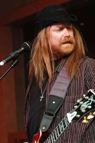 A Person With Long Hair And A Hat Playing Guitar